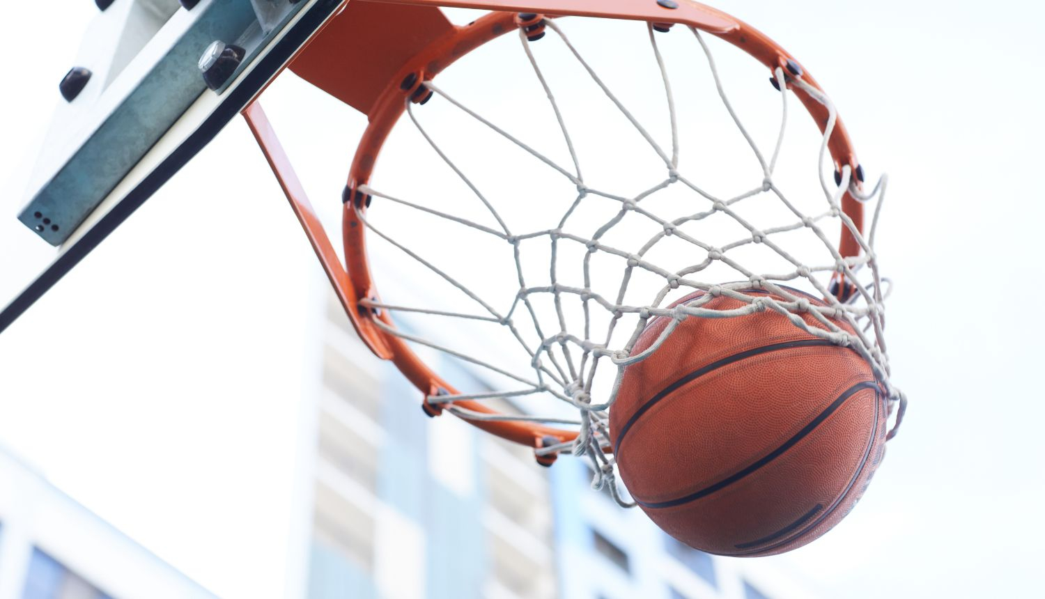 Basketbola bumba iekrīt grozā, fonā gaišas debesis