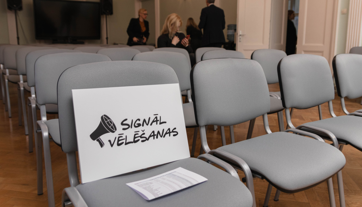 IZM lielajā zālē novietoti krēsli, uz krēsla stāv zīme ar uzrakstu "Signālvēlēšanas"