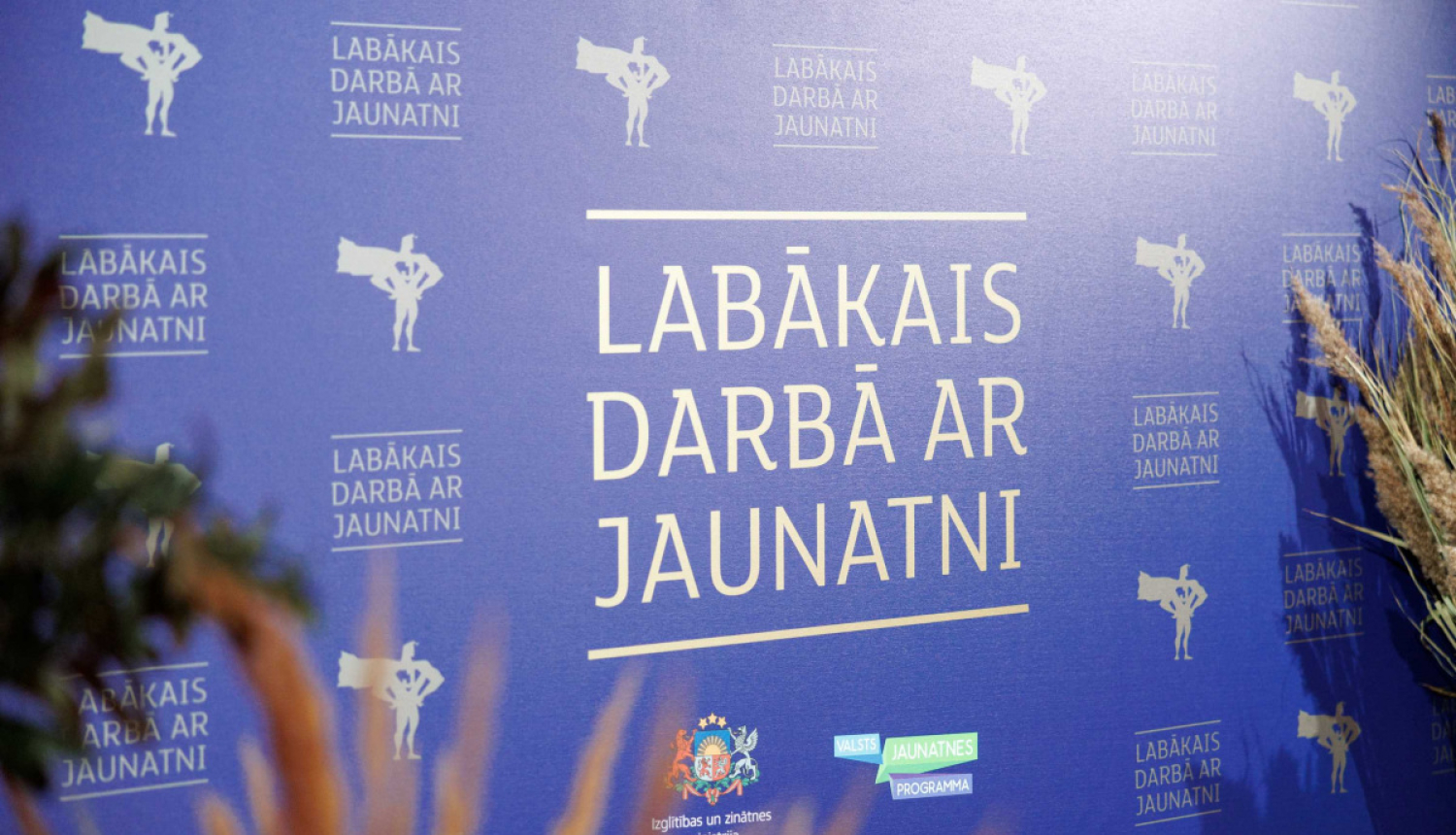 "lABĀKAIS DARBĀ AR JAUNATNI" stends, apkārt stāv augi