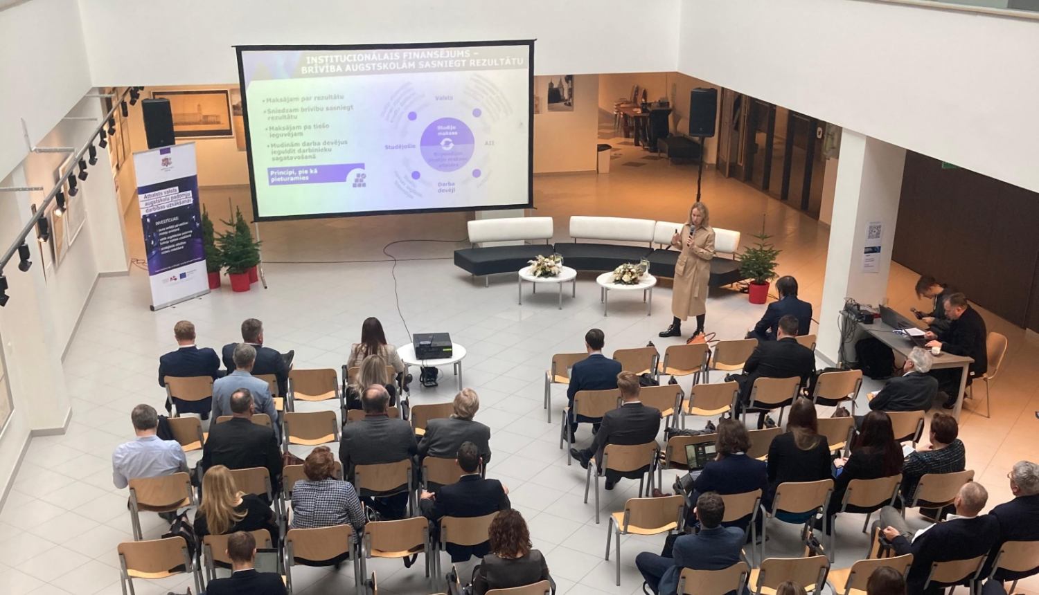 Konference, cilvēki sēž zālē, Diāna Laipniece prezentē