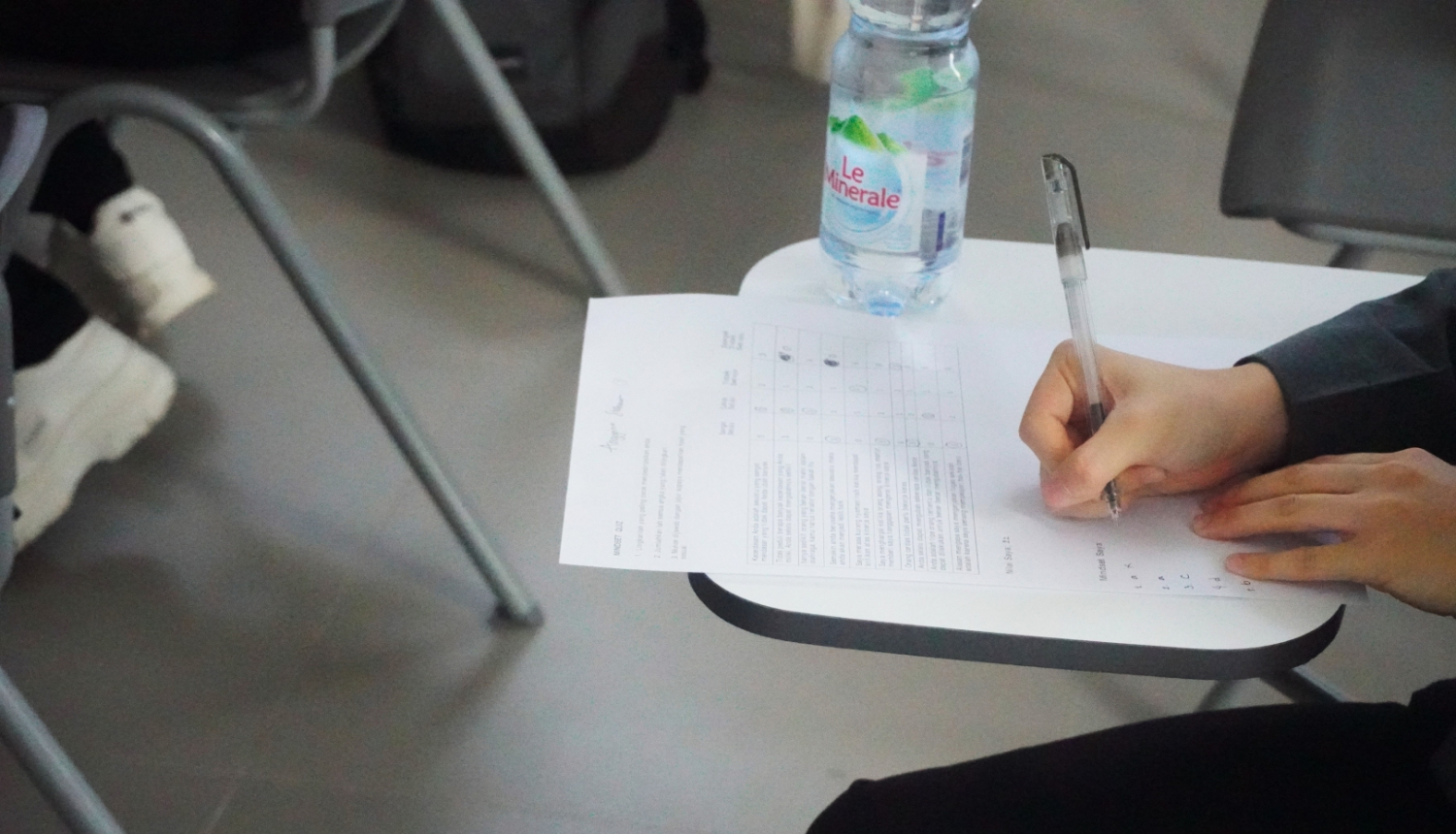 raksta pie galda ar pildspalvu auditorijā