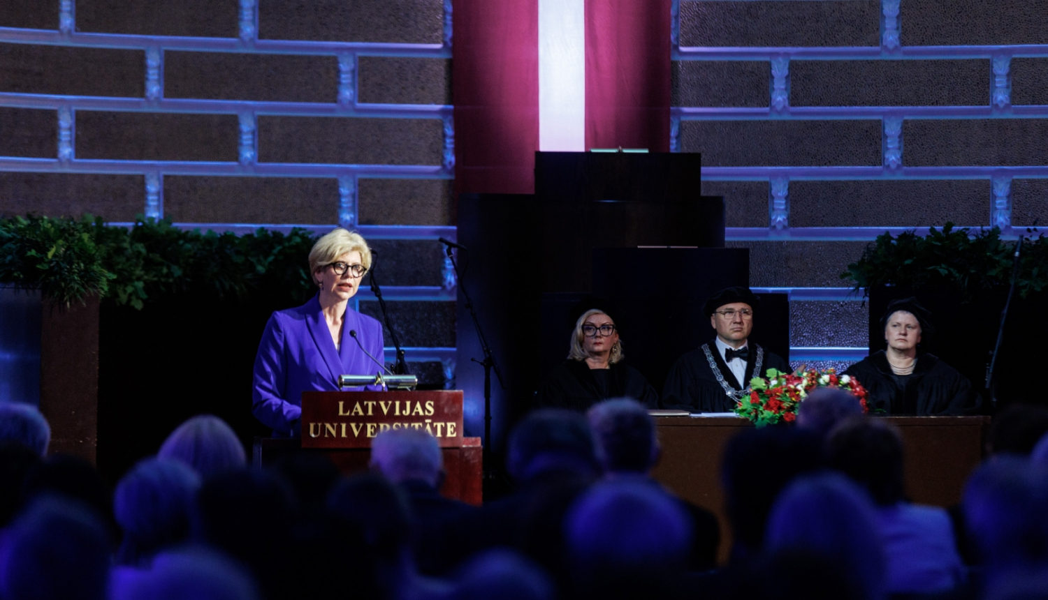 Izglītības un zinātnes ministre Anda Čakša saka uzrunu LU Lielajā aulā, fonā Latvijas karogs