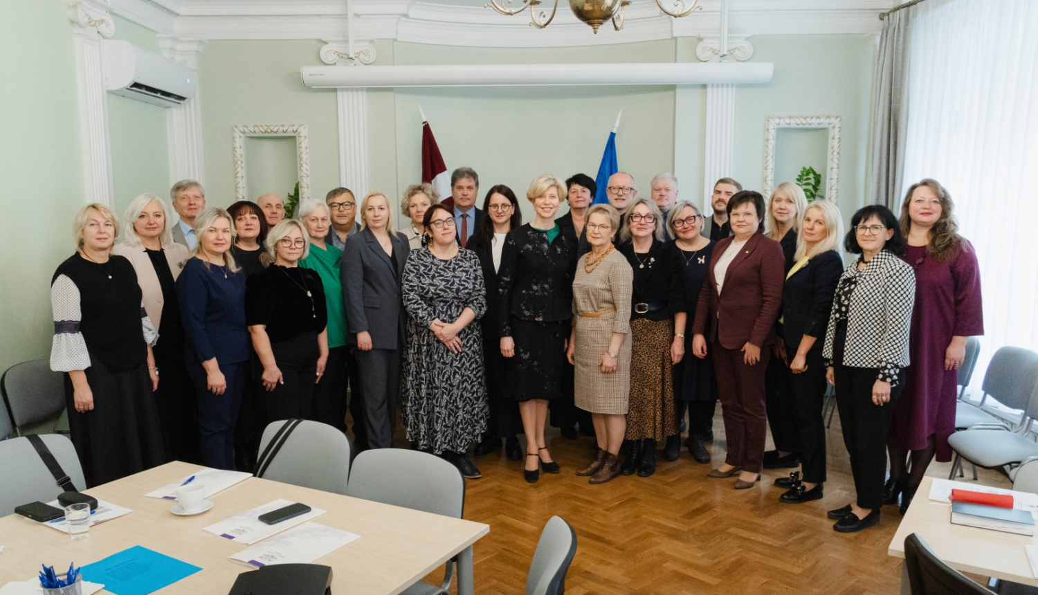 Ministres un skolu direktoru kopbilde pie Latvijas un ES karogiem.