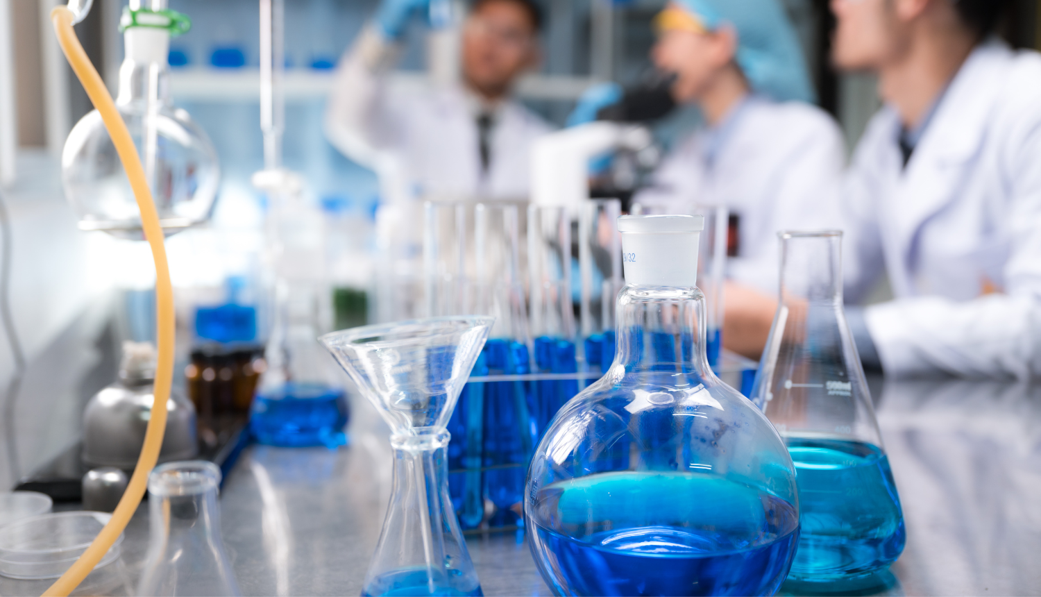 Laboratorija, priekšplānā kolbas ar zilu šķirdrumu