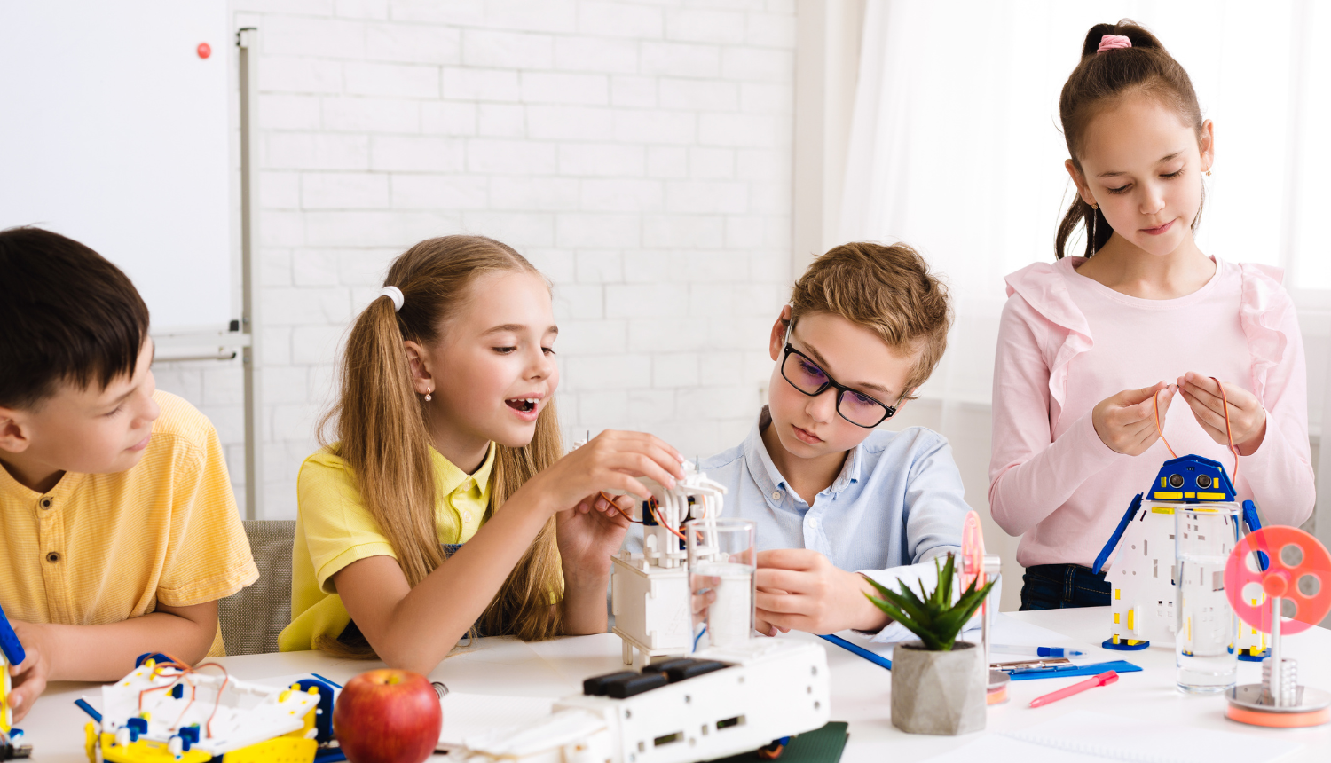 4 bērni pie galda būvē no plastmasas elektroniski darbināmu ierīci