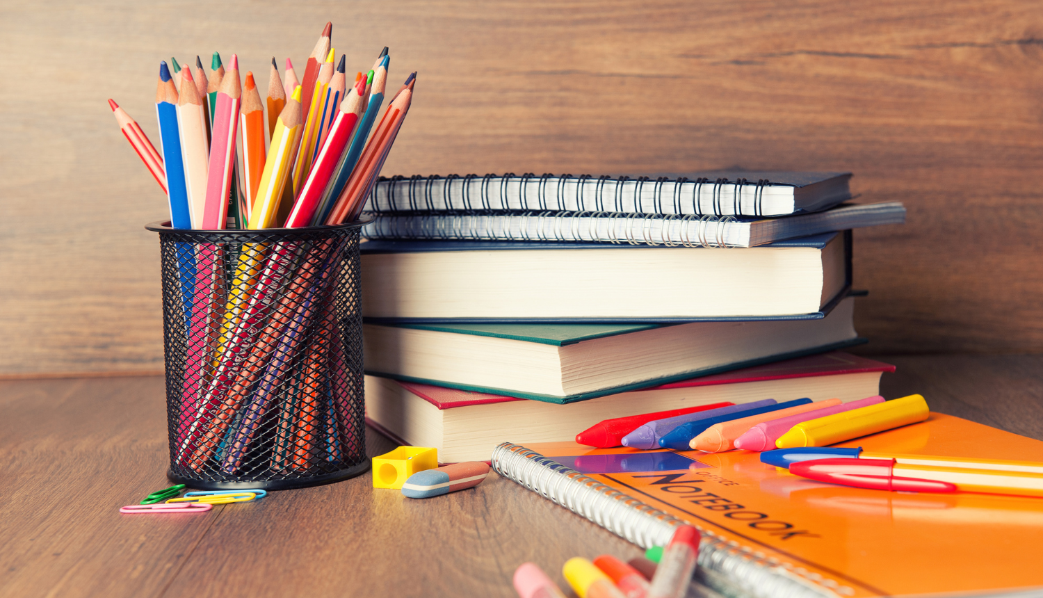 Uz galda stāv grāmatas un zīmuļi melnā glāzē