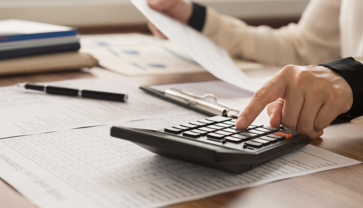 Tuvplānā kalkulators, cilvēks rēķina un trā rokā tur lapu