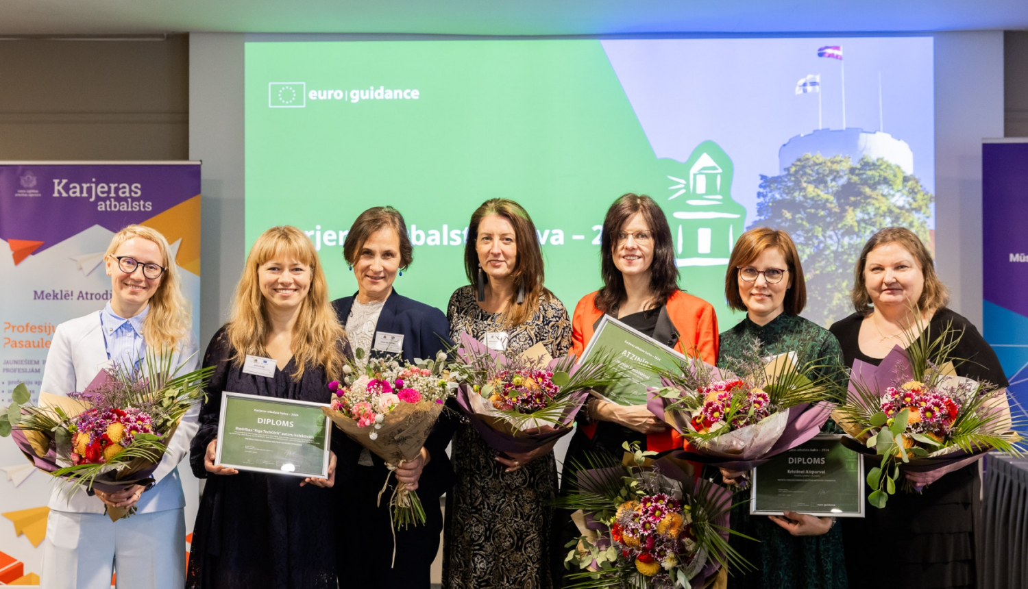 Karjeras atbalsta balvas 2024. gada laureātu kopbilde. Septiņas sievietes ar ziediem rokās.