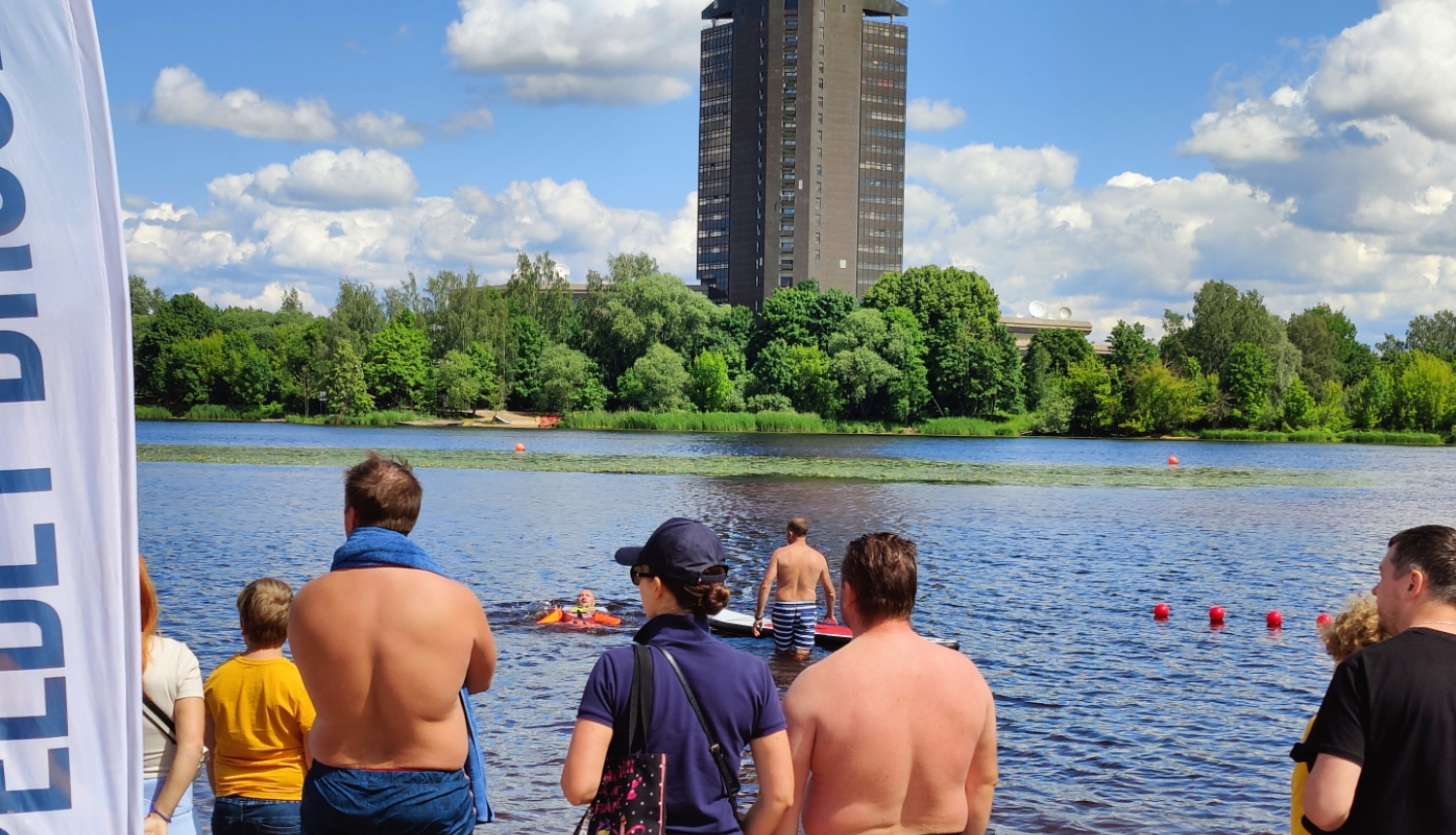 Cilvēki stāv pie Daugavas, viens cilvēks ir glābšanas vestē ūdenī