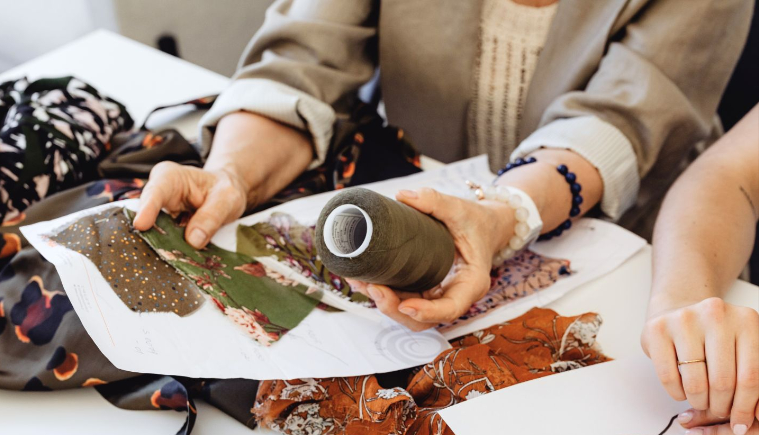 Cilvēki apskata auduma paraugus un diega spolīti, plānojot apģērbu dizainu
