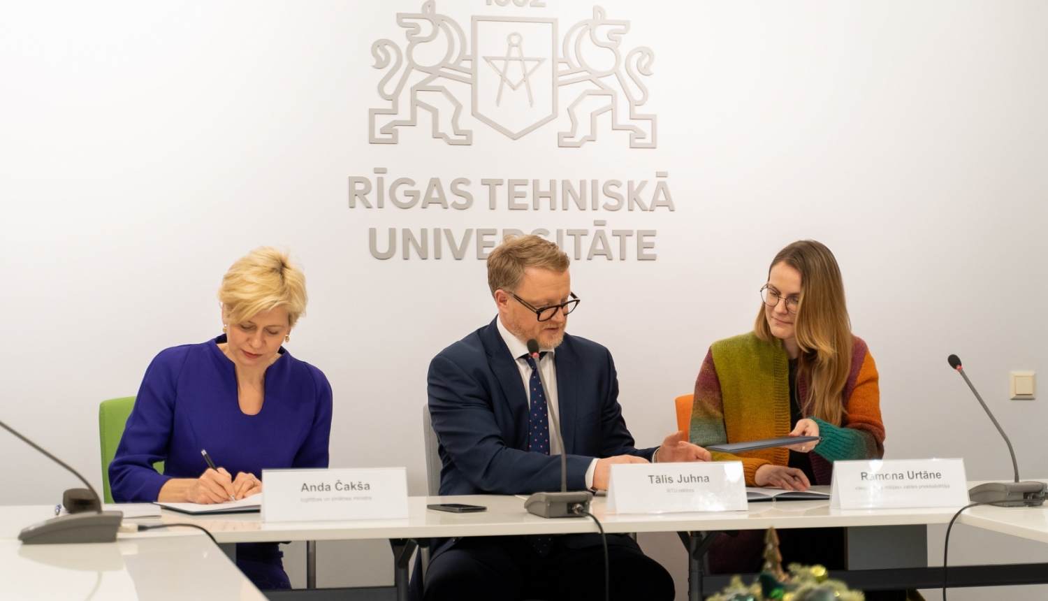 Anda Čakša, Tālis Juhna un Ramona Urtāne sēž pie galda memoranda parakstīšanā