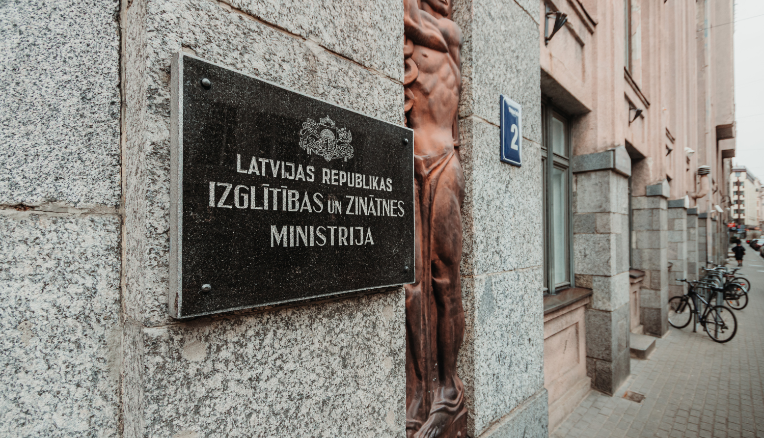 Izglītības un zinātnes ministrijas ieejas durvis, pie sienas plāksne ar IZM logo un uzrakstu