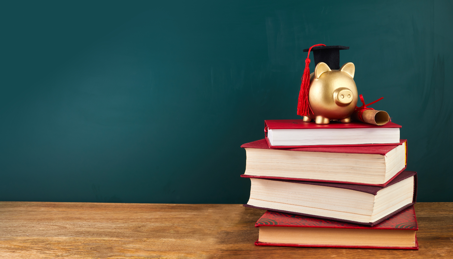 uz galda stāv mācību grāmatas, uz tām stāv krājkasīte ar uzvilktu absolveta cepurīti
