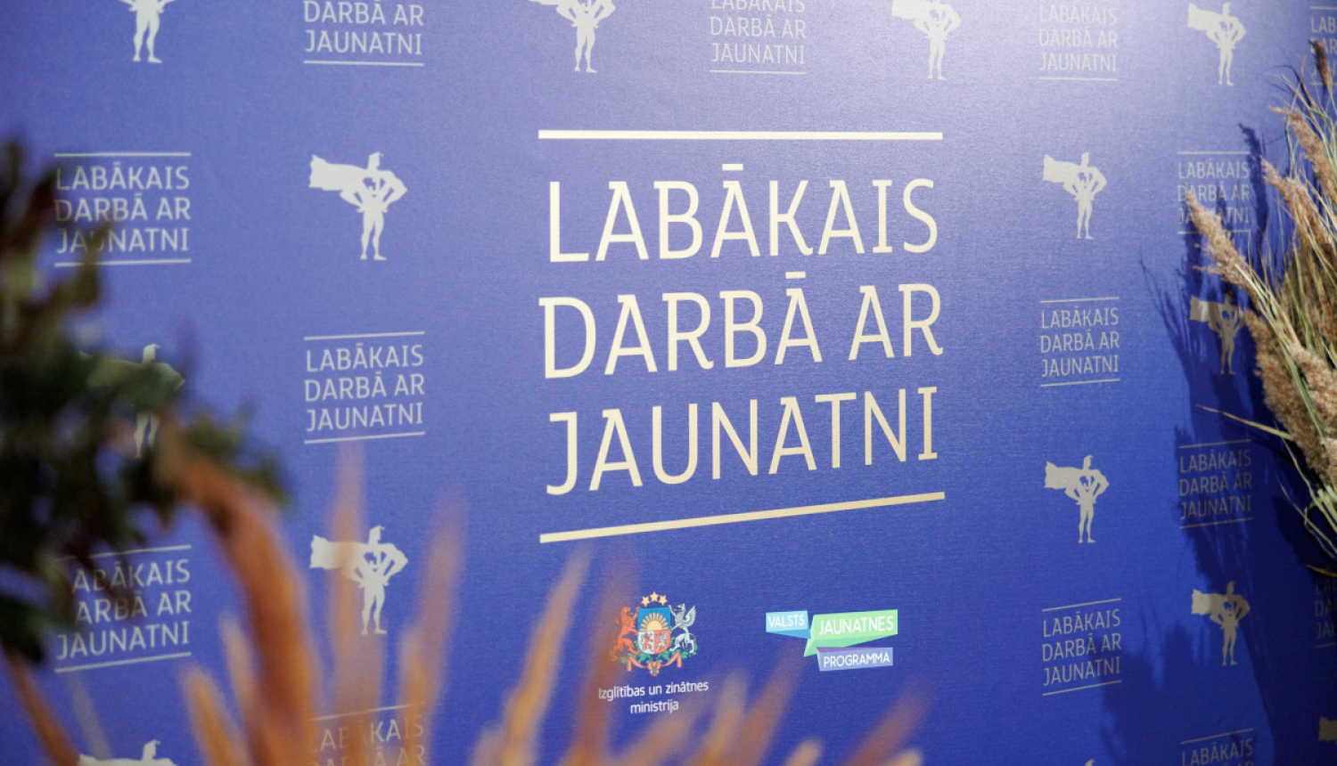 "lABĀKAIS DARBĀ AR JAUNATNI" stends, apkārt stāv augi