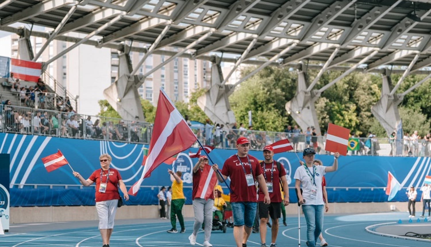Latvijas paralimpiskās komandas pārstāvji pārvietojas pa stadionu ar Latvijas karogiem rokās