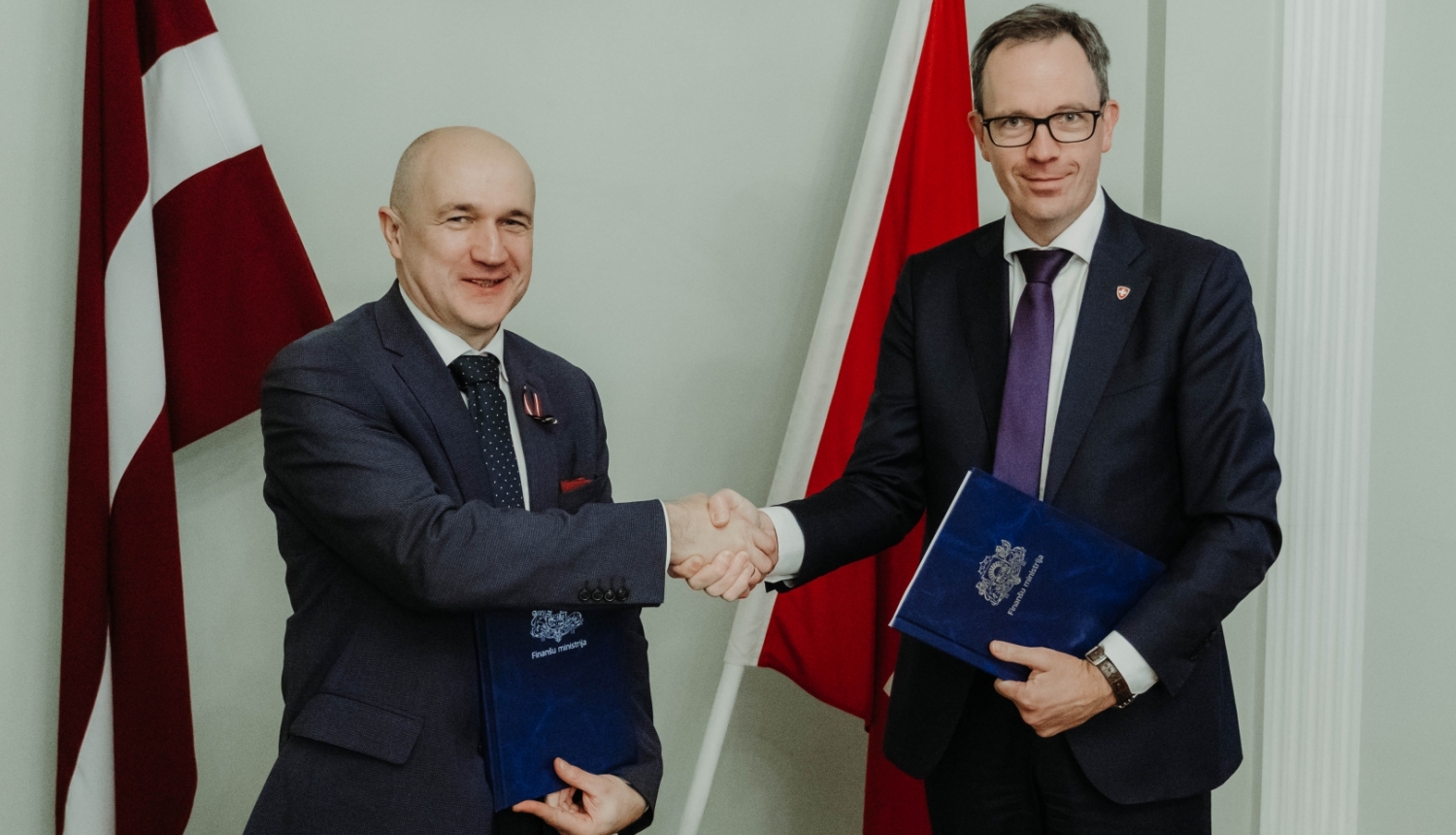 Uz Latvijas un Šveices karoga fona Šveices Konfederācijas vēstnieks Martēns Mišlē un Finanšu ministrijas valsts sekretāres vietnieks ES fondu jautājumos Armands Eberhards spiež viens otram roku