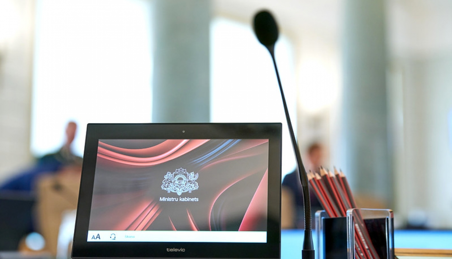 Dators un mikrofons stāv uz galda Ministru kabineta zālē, datora ekrānā redzams Ministru kabineta logotips